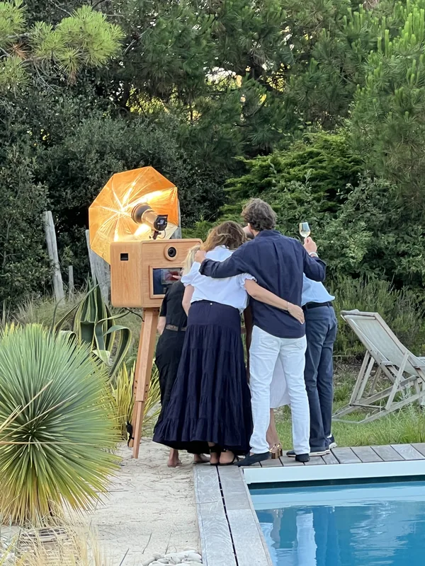 Des invités réunis devant la borne à photo près d’une piscine, dans un jardin
