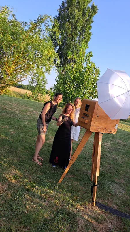 Trois invitées prenant la pose devant la borne à photo avec son parapluie blanc dans un jardin